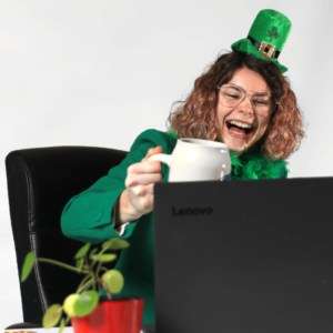 Woman drinking and laughing in St. Patrick's day costume before laptop
